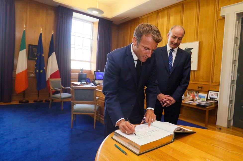 Emmanuel Macron signs a guestbook at Government Buildings in Dublin as Micheál Martin watches on