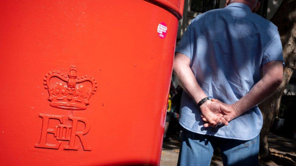 A red post box with a man standing next to it, with the queen's cypher on