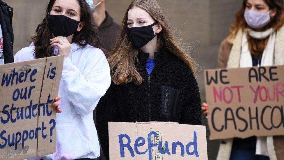 Three students at a protest, holding up signs saying 'Where is our student support?' and 'Refund'