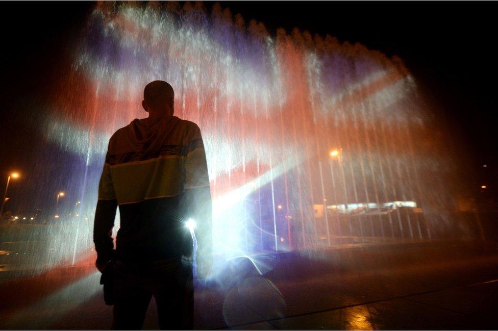 A man stands in front of a fountain illuminated with the colours of the United Kingdom flag in Zagreb, 23 May