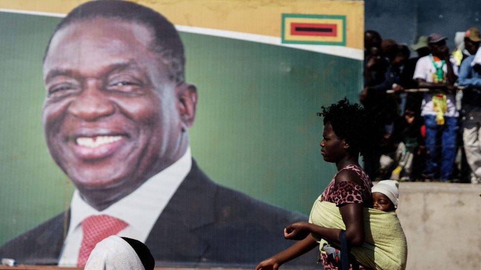 A woman walks in front of a picture of Zimbabwe"s President Emmerson Mnangagwa as ge addresses a ruling ZANU-PF party rally in Bulawayo on June 23, 2018,