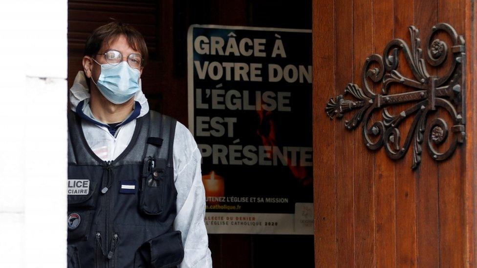 A masked police officer looks out from the doorway of the Notre Dame church in France