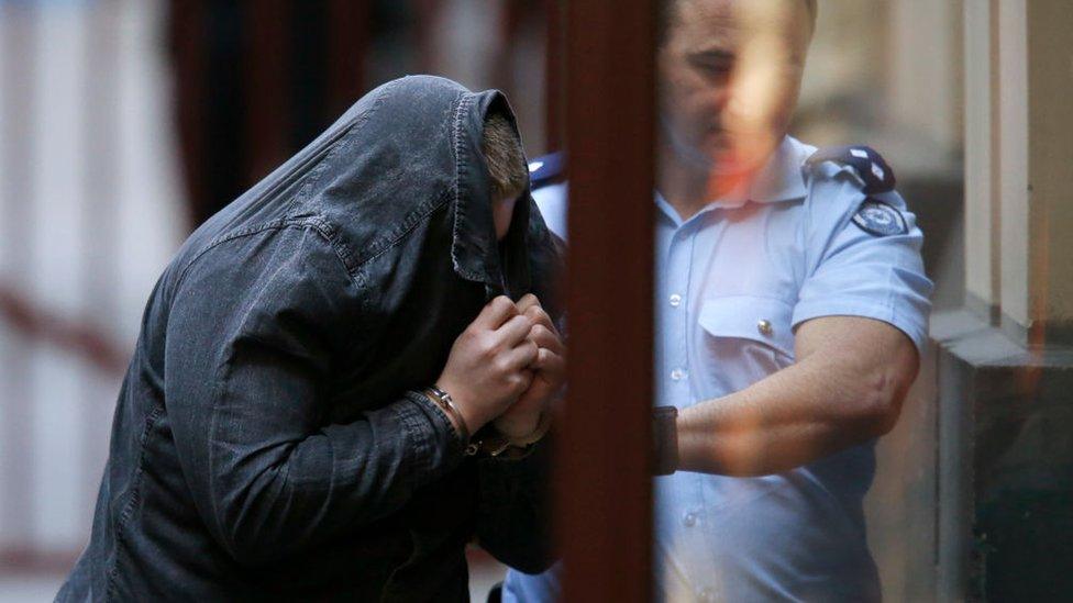 A police officer escorts Jaymes Todd, who is holding a jacket over his face, into the Victorian Supreme Court before his sentencing