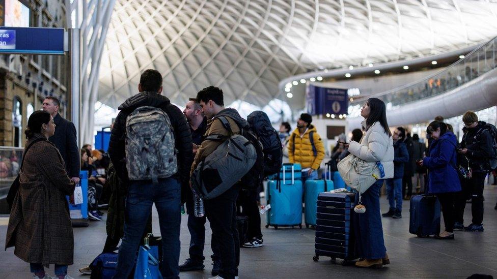 People standing around in King's Cross station with luggage waiting for news of rescheduled train services