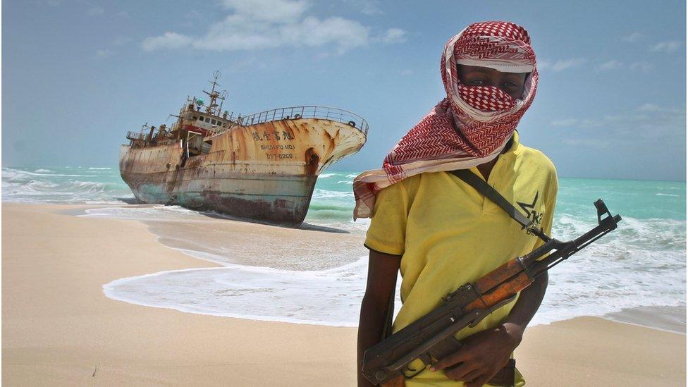 Masked and armed Somali pirate Hassan stands near a Taiwanese fishing vessel washed ashore in Hobyo, Somalia. 23 Sept 2012.