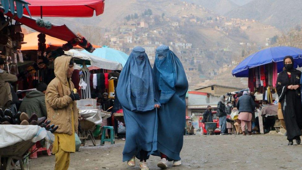 Afghan burqa-clad women walk past a market at Fayzabad district, in Badakhshan province