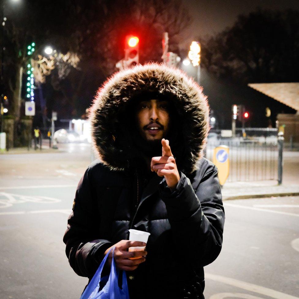 An image of a man with a big furry hood pointing at the camera