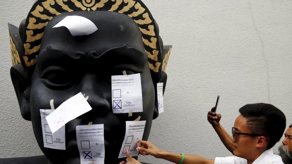 An opposition student attaches a mock ballot with the option "No" to a statue during a protest against the military-backed draft constitution in Bangkok