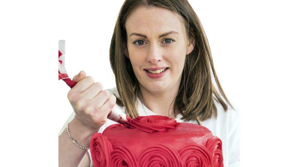 Imelda smiles while icing a bright red cake with roses