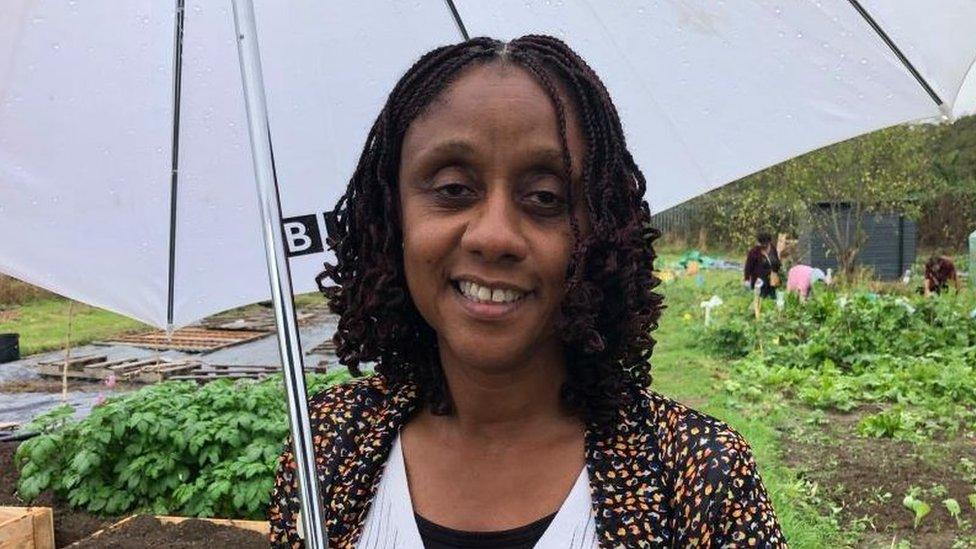 Woman with long dark hair holds an umbrella in an allotment