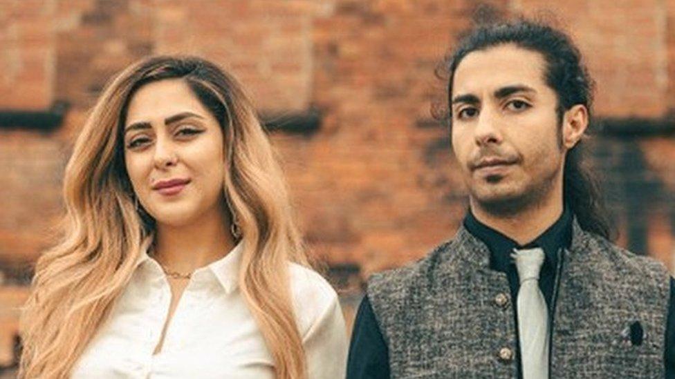 Iranian musicians Nasim Heidari and Omid Shir Mohammadi stand in front of a red brick wall