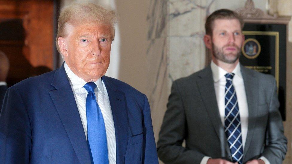 Donald Trump in blue suit with blue tie, Eric Trump in grey suit.