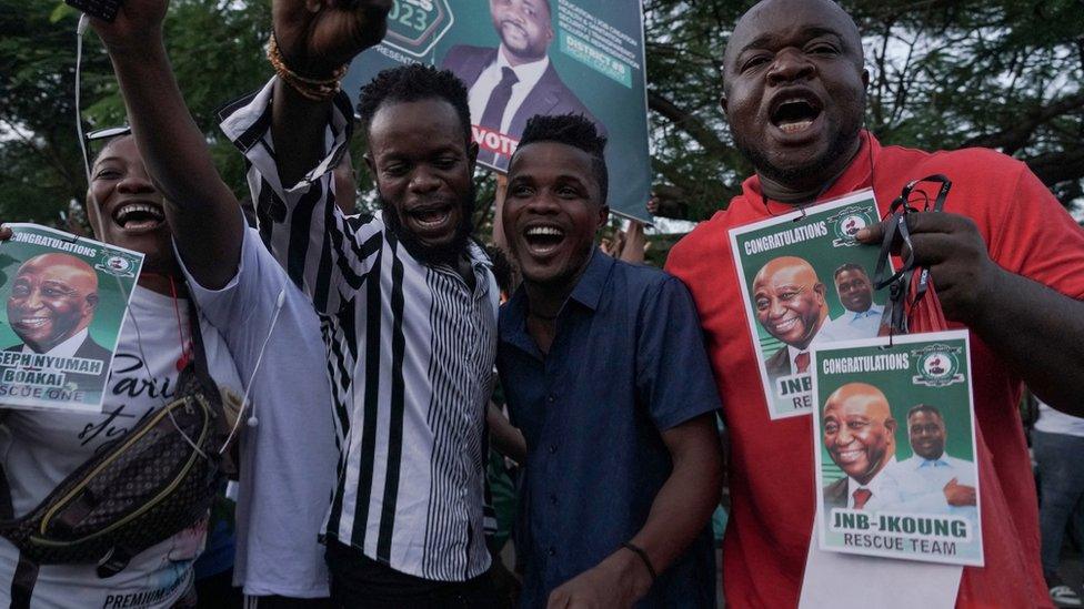 People smiling and celebrating with posters of Joseph Boakai