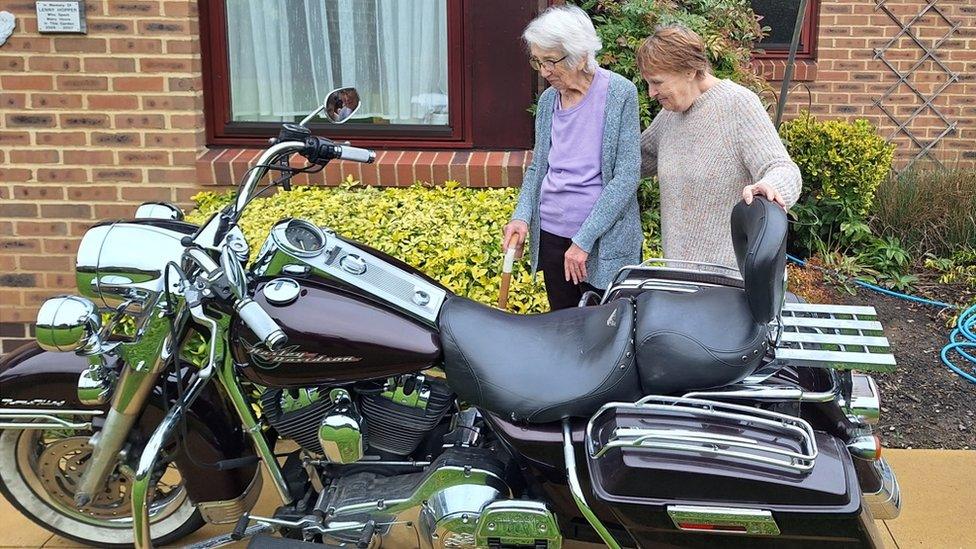 Two older women stand alongside a large motorbike