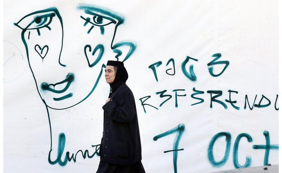 A Romanian Orthodox nun passes by a graffiti symbolizing the crying face of a LGBT community member on 5 Oct