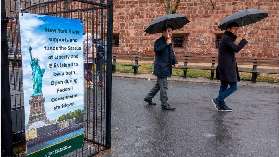 People walk past a sign announcing that New York funds are keeping the Statue of Liberty and Ellis Island open for visitors on January 5, 2019, in New York