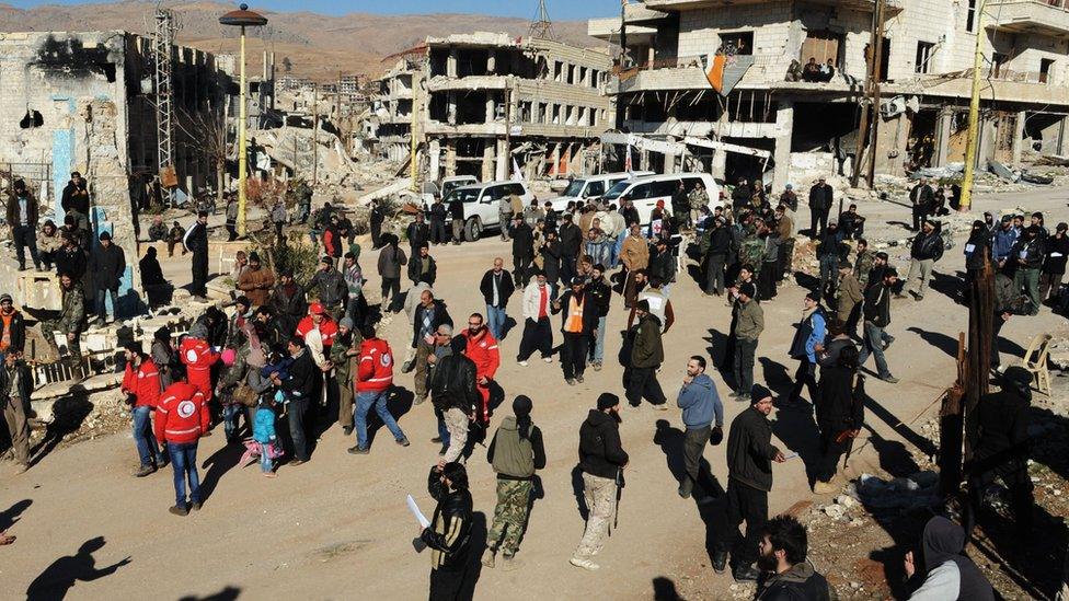 Syrian opposition fighters and their families gather at a square surrounded by damaged buildings, as they prepare to evacuate Zabadani town, Syria (photo from Syrian official news agency, Dec. 28, 2015)