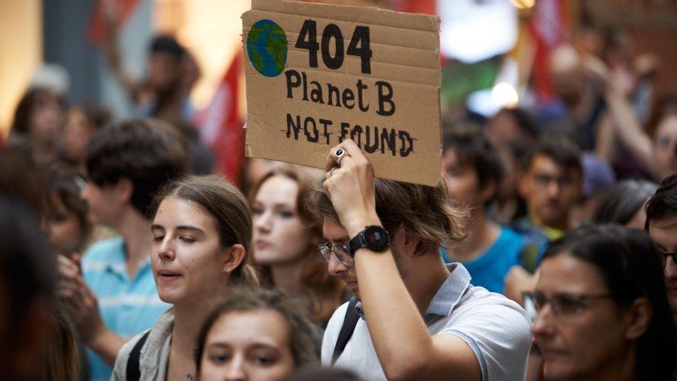 Person holding "404 planet not found" cardboard protest sign