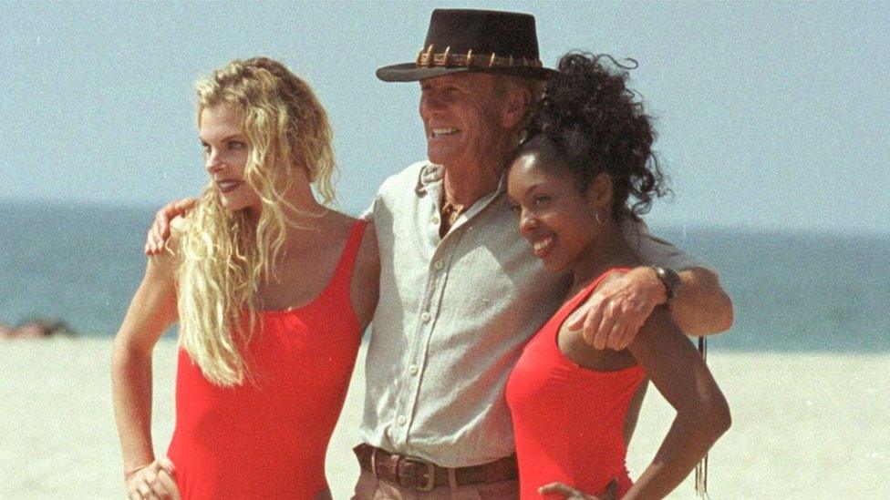 Paul Hogan poses with two women in swimsuits during filming for the 2001 film Crocodile Dundee in Los Angeles