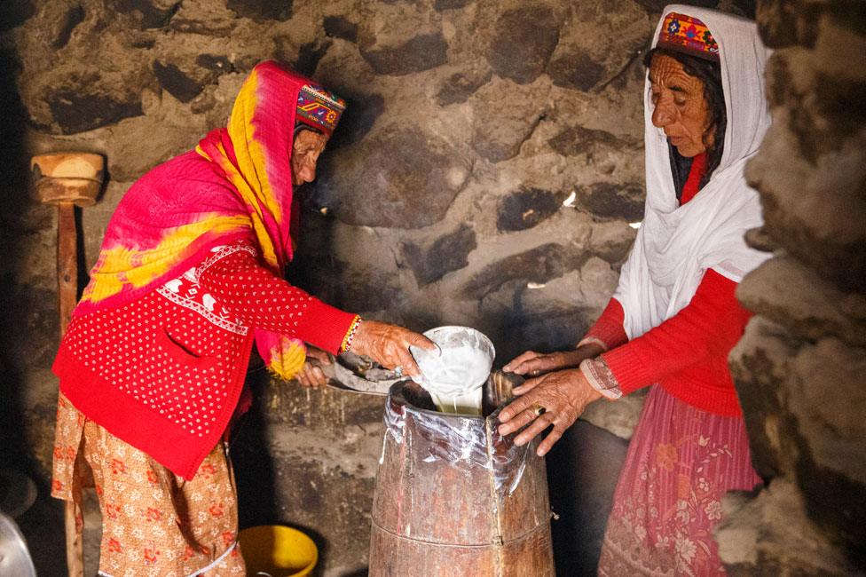 Annar (left) and Thai Bibi (right) inside a hut pouring yoghurt into a traditional wooden drum to make butter