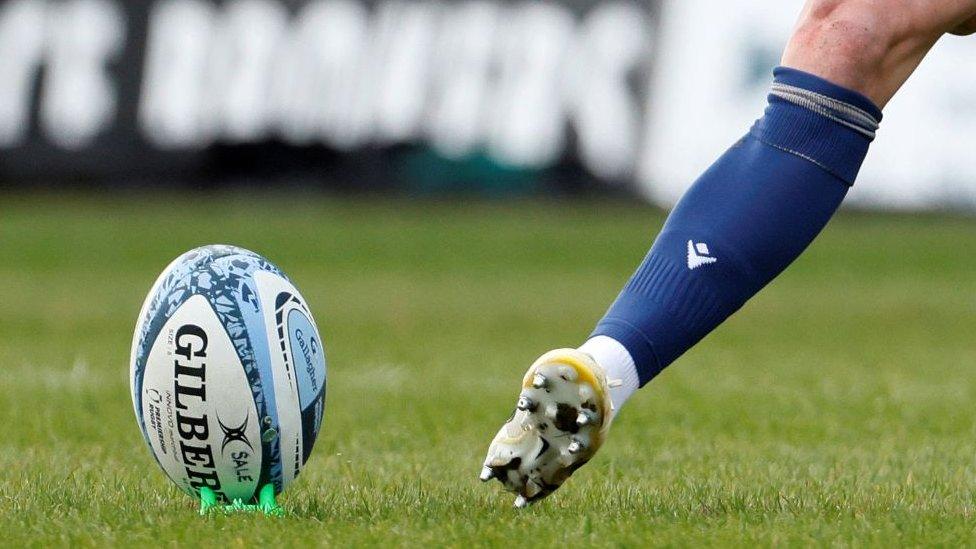 Close up shot of a blue and white rugby ball on a pitch about to be kicked