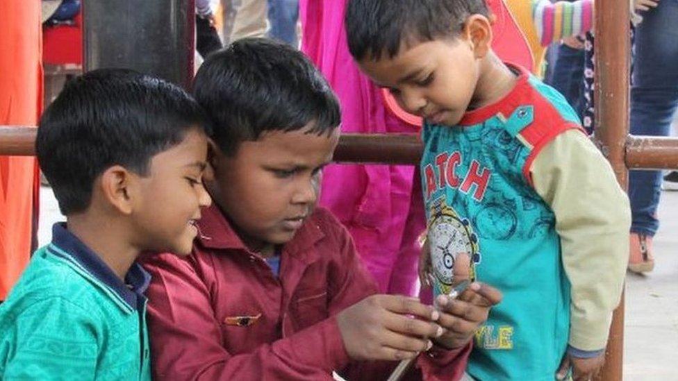 Indian children in Delhi watch something on a mobile phone.