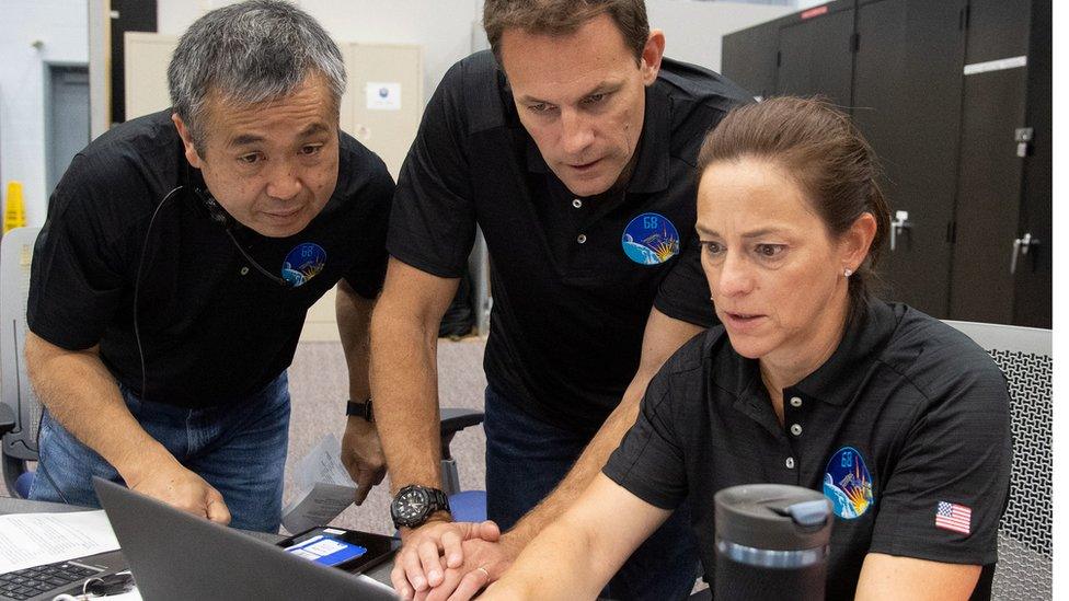 Nicole Mann, Josh Cassada and Koichi Wakata gather around a laptop during training