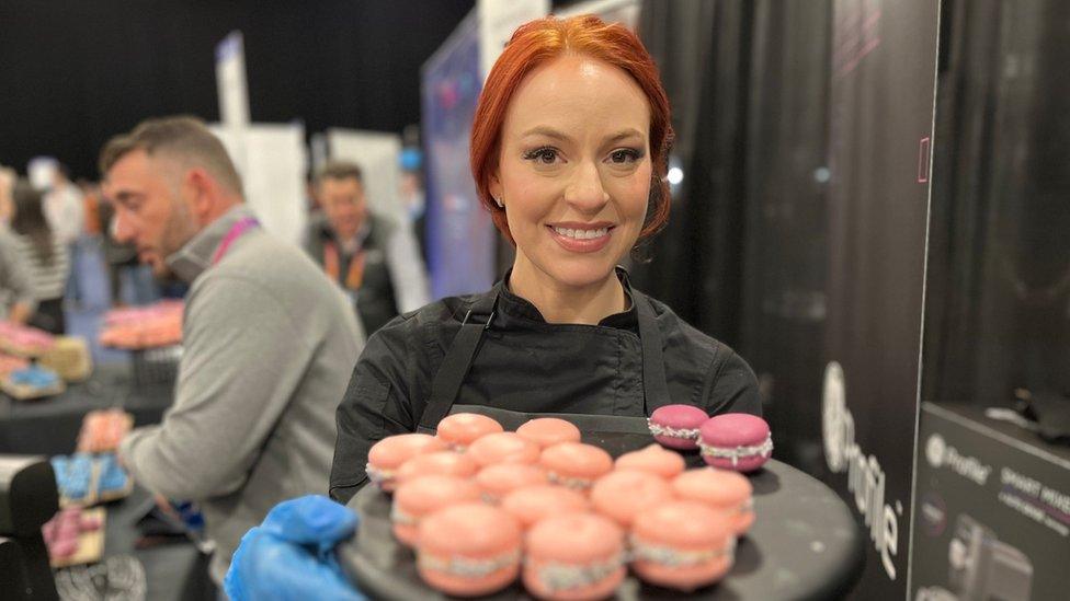 A woman showing off a plate of uniform, colourful macarons