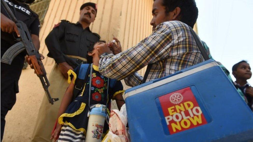 Pakistani policemen stand guard as a health worker administers polio drops to a child during a polio vaccination campaign after a day of an attack by gunmen in Karachi on April 21, 2016.