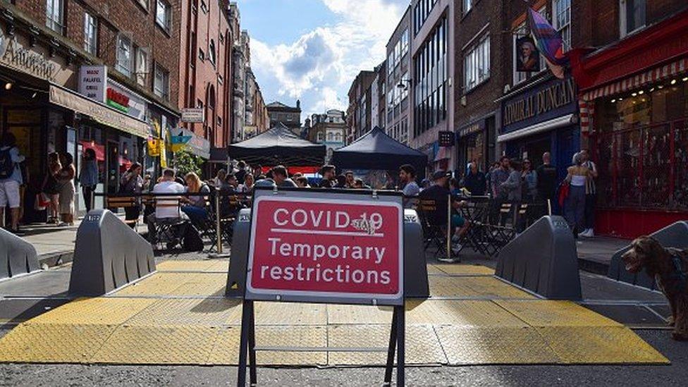 Covid restriction sign on street with busy restaurants