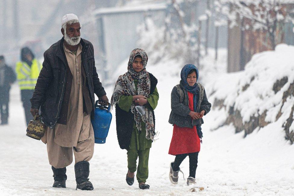 A man carrying gas canisters walks next to children along a street during snow fall in Kabul on January 11, 2023.