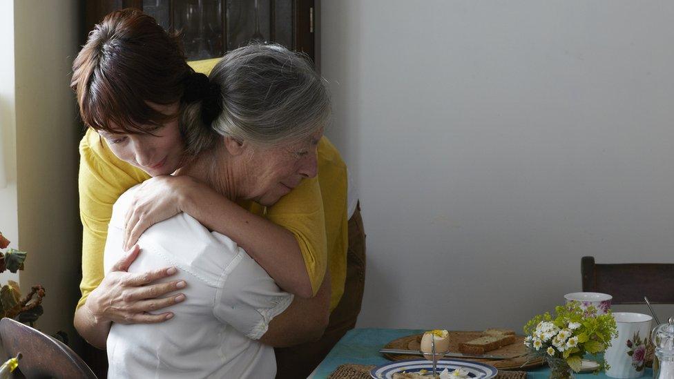 Elderly woman hugging a younger woman.