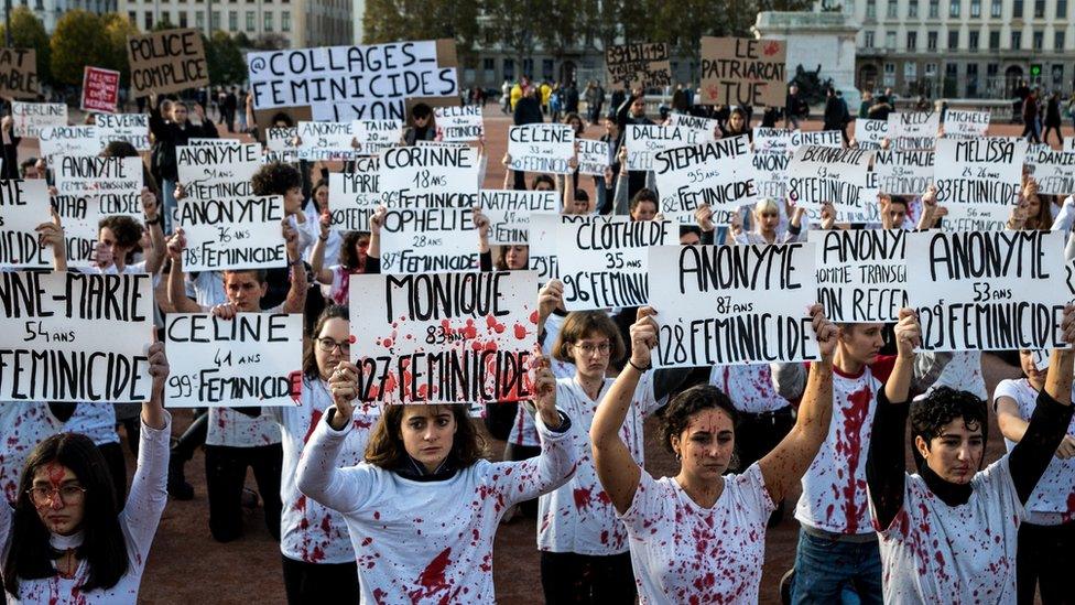 Protestors stand with signs while covered in red splatter that resembles blood