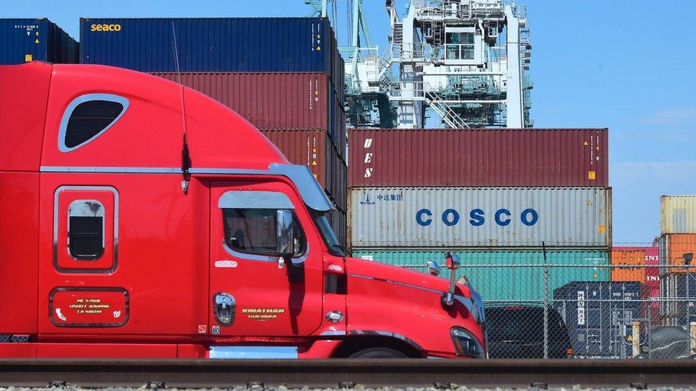 In this file photo taken on July 6, 2018 a container delivery truck passes containers stacked at the Port of Long Beach in Long Beach, California including one from COSCO, the Chinese state-owned shipping and logistics company.