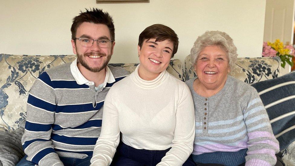 Bryony, Matt, and Janet sat on the sofa, smiling at the camera