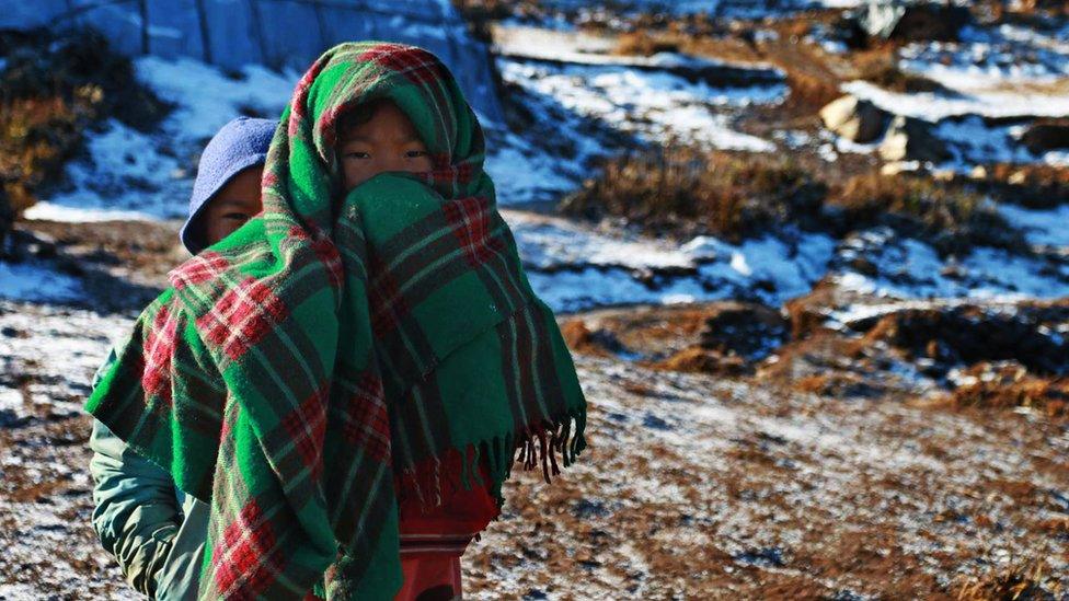 Two young Nepalis stand among temporary shelter in the Nepalese village of Laprak, 21 January 2016