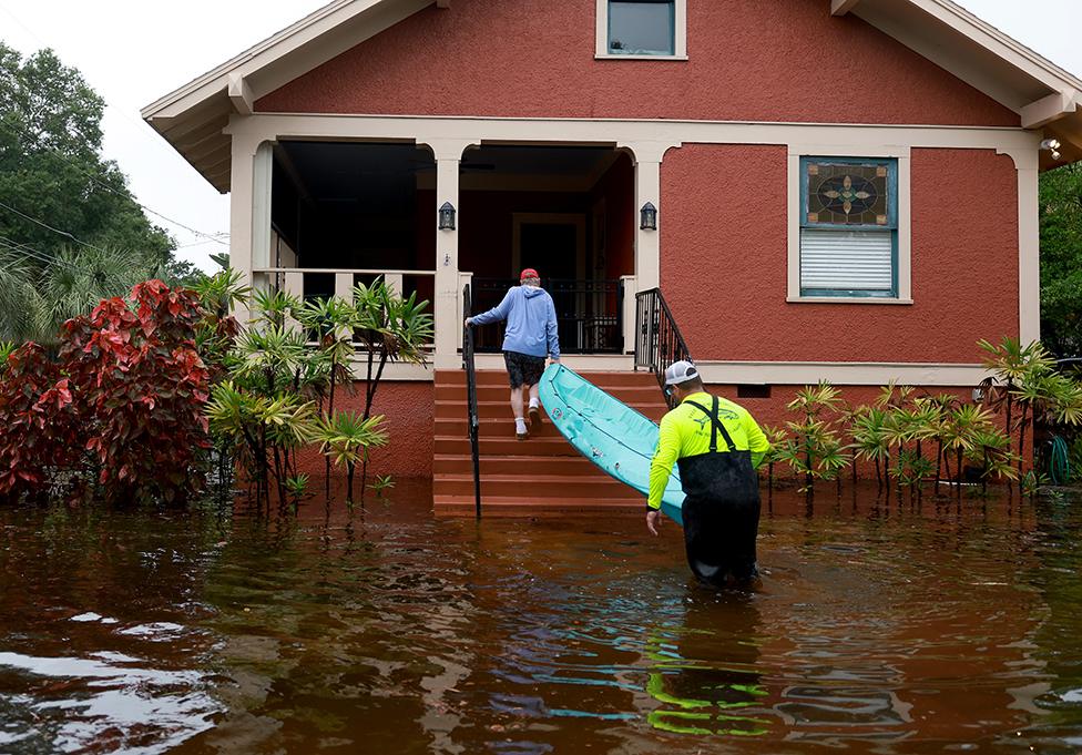 People carry a kayak onto his porch through the flooded streets caused by Hurricane Idalia passing offshore on August 30, 2023 in Tarpon Springs, Florida