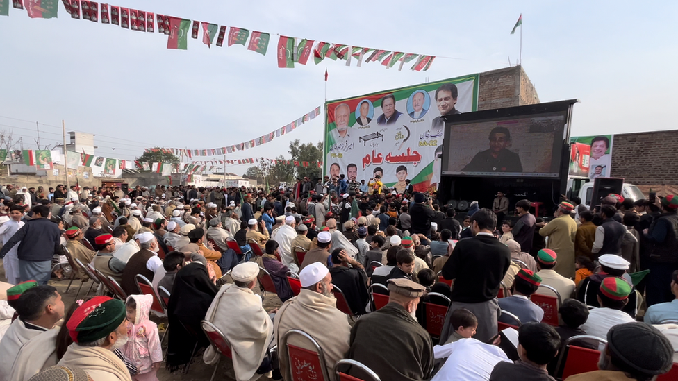 People at a rally for Atif Khan in Khyber Pakhtunkhwa watch him speak on a big screen on the back of a truck 3 Feb 2024