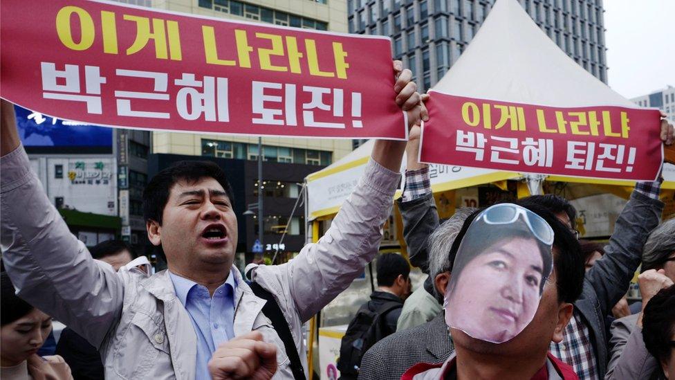 A protester (right) wears a cut-out photograph of Choi Soon-sil while another demonstrator holds a banner reading "President Park Geun-hye's resignation" in Seoul on 27 October 2016