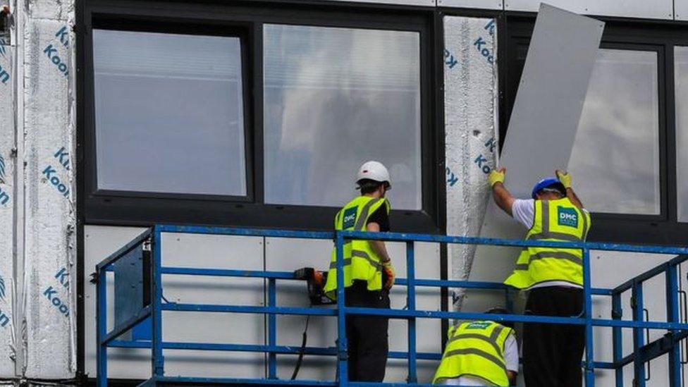 Builders remove cladding from a high rise building