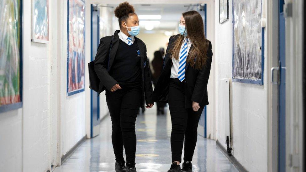 Two schoolgirls talking in a school corridor while wearing face masks