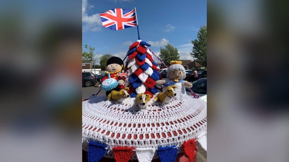 A knitted post box topper showing the Queen, corgi dogs and a tree in red, white and blue in Gravesham