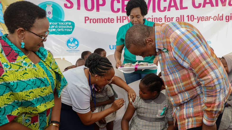 Kenyan President Uhuru Kenyatta looks on a nurse injects a girl