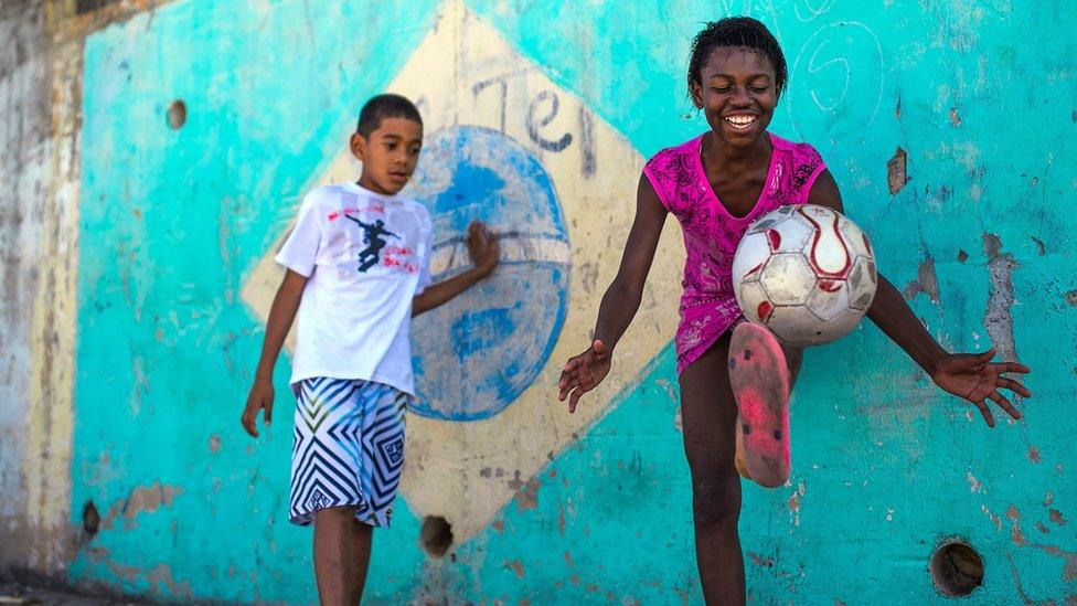 A boy and girl play football in the Chacara do Ceu favela