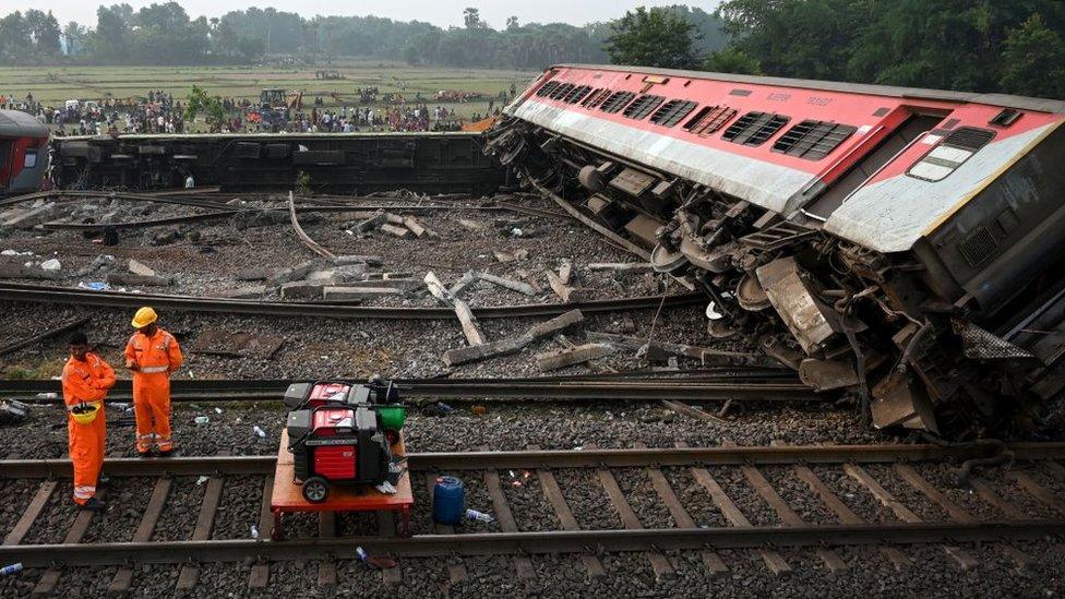 Rescue workers stand near a damaged carriage at the accident site