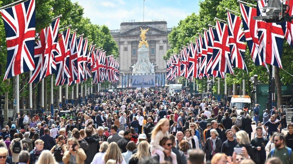 Crowds of sightseers walk under Union Jack flags lining the Mall leading to Buckingham Palace