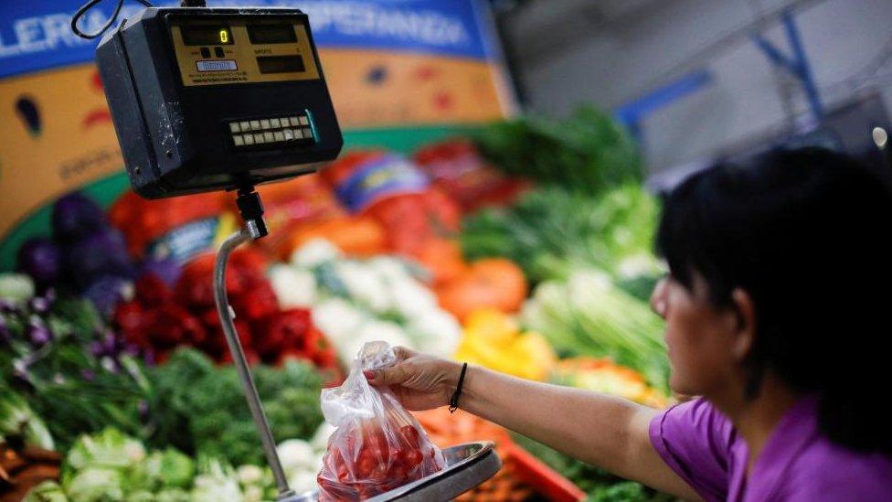 A vegetable seller weights tomatoes at a greengrocery store in a local market, as Argentina's annual inflation rate tore past 100% in February