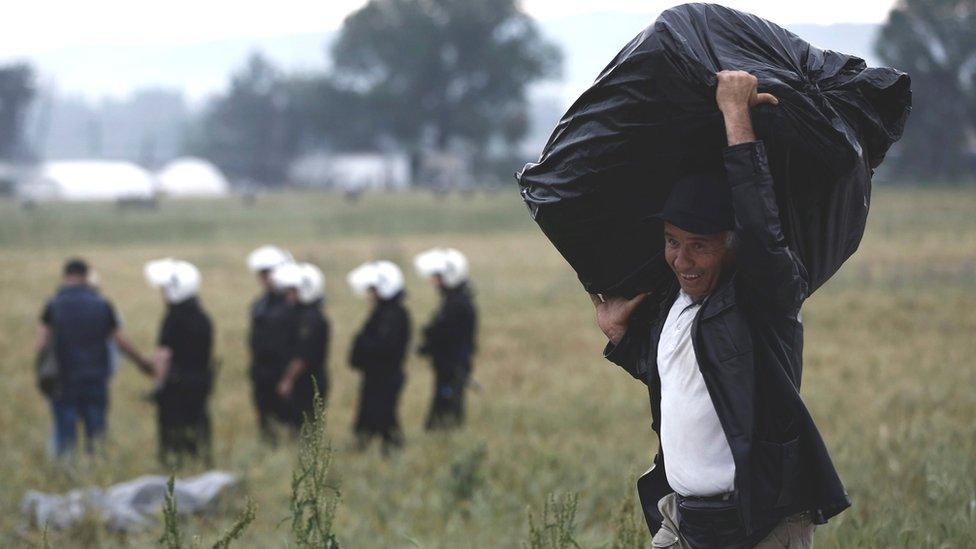 Migrant carries his belongings as police clear Idomeni camp, Greece, on 24 May 2016