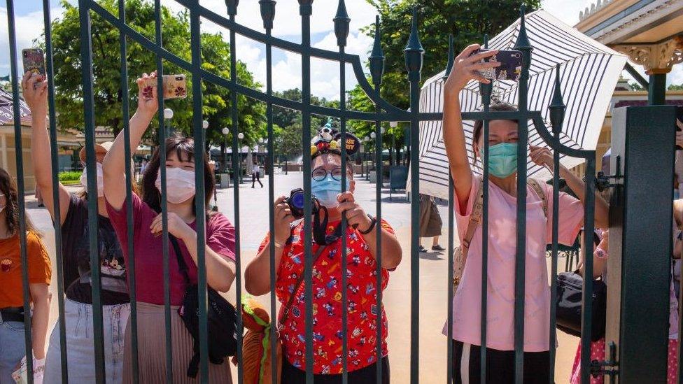 Hong Kong Disneyland visitors wearing protective face masks take photographs behind a fence.