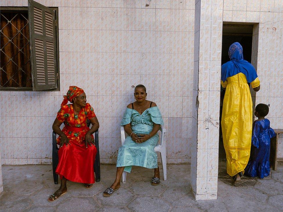 Khady Diouf wears a red dress and Aissatou Cissé is in blue. They sit outside on chairs